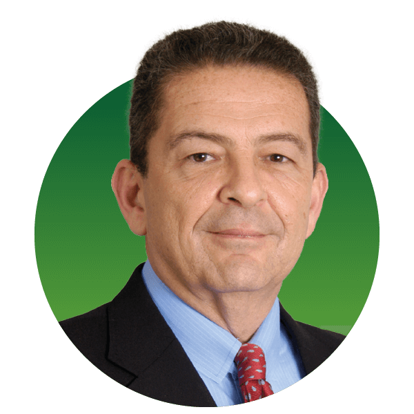 Portrait of a man in a suit with short hair against a green gradient background. He is wearing a blue shirt and a red patterned tie, looking directly at the camera with a neutral expression.