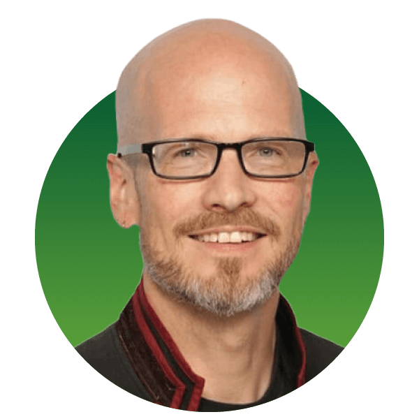 A bald man with glasses and a beard is smiling, set against a green background. He is wearing a dark jacket with a red trim.